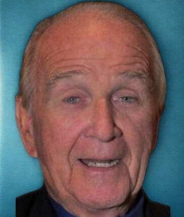 Elderly man smiling against a blue background.
