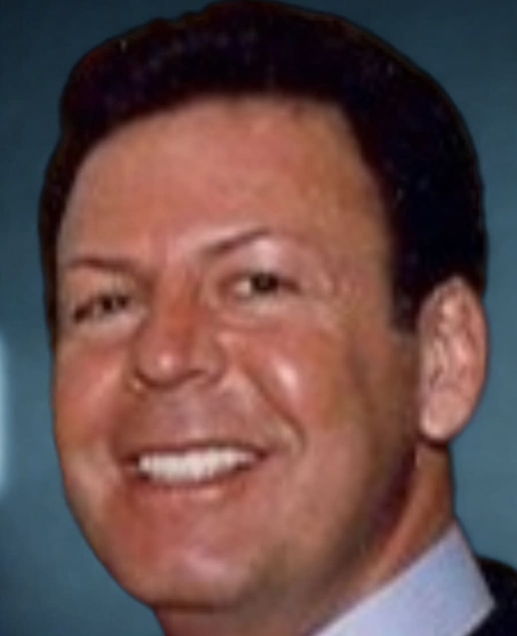 Smiling man with dark hair, blue background.
